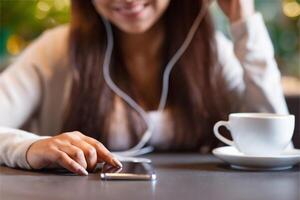 Cropped of girl is seated at a table, wearing headphones and listening to music. Beside her, a cup of coffee is placed on the table. She appears focused on enjoying her music and drink. photo