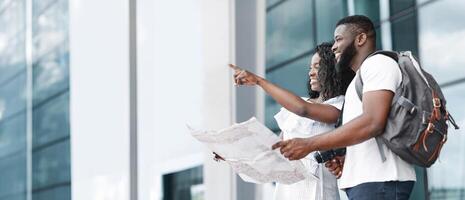 African American couple stand outside a building with modern architecture. The woman is pointing to the right, while the man is holding a map and smiling, copy space photo