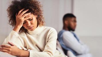Frustrated afro couple having misunderstanding in relationship, avoiding talking to each other, sitting on sofa photo