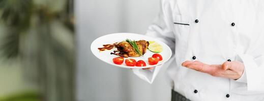 Unrecognizable Chef Guy Holding Plate With Roasted Chicken Presenting Dinner Standing In Kitchen. Cropped, Panorama, Selective Focus photo