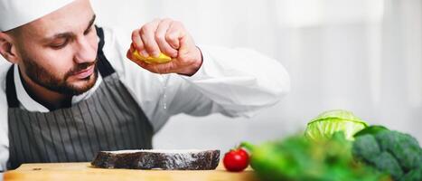 Cooking Fish. Chef Man Squeezing Lemon Juice On Salmon Steak Standing In Restaurant Kitchen. Selective Focus photo