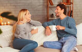 Happy Couple Enjoying Conversation Having Coffee Sitting On Couch At Home. Selective Focus photo