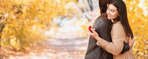 Marriage proposal at autumn forest. Happy woman looking at proposal ring while hugging her boyfriend, copy space photo