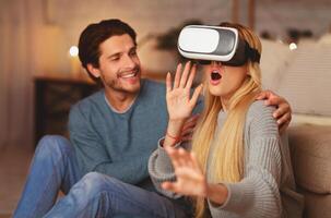 Excited Spouses Using VR Headset Experiencing Virtual Reality And Having Fun Sitting Indoor. Modern Home Entertainment. photo