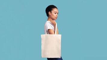 No Plastic. Black Girl Holding Blank White Eco Bag Posing Over Turquoise Studio Background. Panorama, Empty Space photo