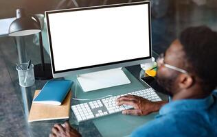 Unrecognizable black businessman using computer with empty blank screen, sitting at workplace in office, offering space for mockup on monitor. Male CEO showing place for online ad photo