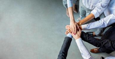 Teambuilding And Togetherness. Unrecognizable Business People Holding Hands Standing In Modern Office. Panorama, Above View, Empty Space photo