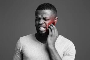 Sad afro man having gum problems, touching his cheek, white studio background, tooth disease concept photo
