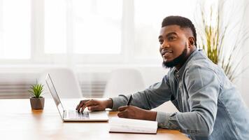 First day in new office. African american man taking notes from laptop on his first day of internship and listening advices of his colleagues photo