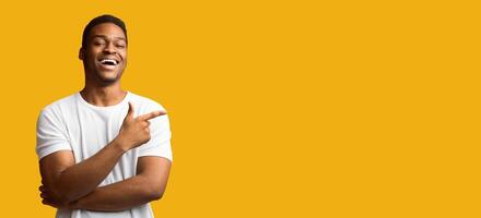 Advertisement Concept. Happy black guy pointing at copy space isolated over yellow studio background, panorama photo