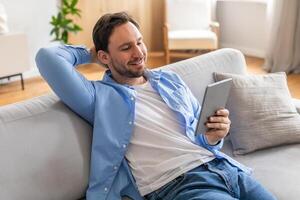 A man is casually sitting on a couch, engrossed in using a tablet device. He appears focused as he interacts with the screen, showcasing modern technology in everyday life. photo
