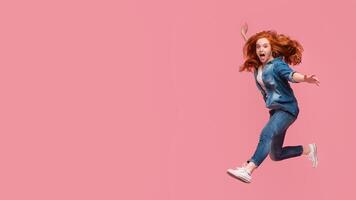 Activity and happiness. Excited redhead woman having fun, jumping on pink studio background photo