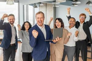 A group of diverse business professionals celebrates a successful project in their modern office. The team is ecstatic, with smiles and raised fists, expressing their shared joy. photo