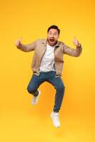 A man is captured mid-jump, with his hands raised above his head in the air. He appears to be in a moment of excitement or celebration, leaping energetically. photo