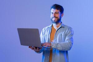A man sitting at a desk is smiling while interacting with a laptop computer. He appears engaged and focused on the screen, possibly working or communicating with others online. photo