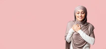 Gratitude concept. Thankful muslim girl in hijab keeping both palms on chest, expressing appreciation over pink studio background with copy space photo