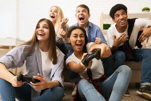 A group of multiethnic friends are gathered around a couch, engrossed in playing games together. They are sitting closely together, holding game controllers, and focused on the screen. photo