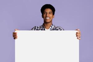 Excited afro guy showing blank banner with free space for your text, pink background photo