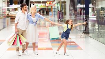 Family Shopping In Mall. Little Girl Pointing Finger Showing Something In Store Window To Her Parents Walking In Hypermarket. photo