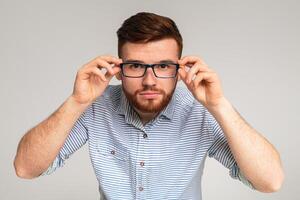 Young redhaired guy try on glasses in front of camera on studio background, panorama photo