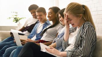 A joyful gathering of five multiethnic teenagers as they sit closely on a comfortable couch, engaging in cheerful conversation, studying at home photo