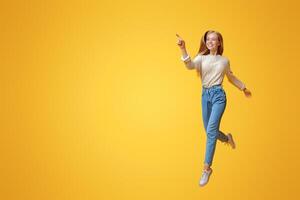Look there. Cheerful teen girl jumping and pointing aside on copy space over orange background photo