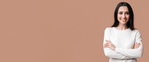 Beautiful millennial girl. Portrait of confident smiling woman posing to camera with folded arms over yellow studio background with free space photo