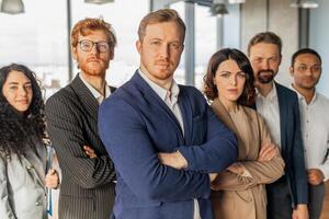 A diverse group of business professionals stand in a modern office setting, exuding confidence and professionalism. The team, consisting of six individuals, is dressed in formal attire photo