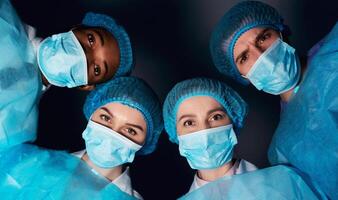 Patient pov. Team of surgeons looking at patient after performing operation in dark room photo