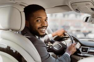 African American man in a suit is driving a car while smiling and looking over his shoulder. He appears to be enjoying his drive. photo