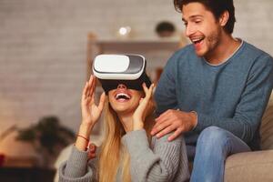 Excited Couple Using Virtual Reality Glasses Playing Videogame Having Fun At Home. Selective Focus photo