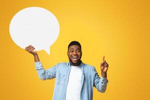 I have an idea. Inspired african american man holding empty speech bubble on yellow studio background, copy space photo