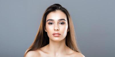 A young woman with long, brown hair and a neutral expression looks straight into the camera. She is posing against a simple, grey background and exudes a calm, elegant demeanor. photo