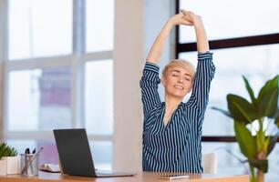 Break At Work. Entrepreneur Lady Stretching Hands With Eyes Closed Working At Laptop Sitting In Modern Office. Selective Focus photo