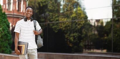 Happy smiling african american student guy with backpack and workbooks over university background, looking at camera and smiling photo