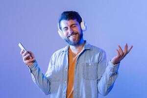 A man with headphones on his ears is seen holding a cell phone in his hand. He seems focused on the screen, possibly listening to music or a phone call. The background is not visible in the frame. photo