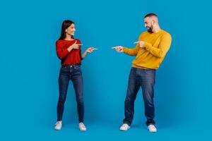 A man and a woman standing facing each other, both pointing accusingly at each other with serious expressions. They seem to be engaged in a heated discussion or argument. photo
