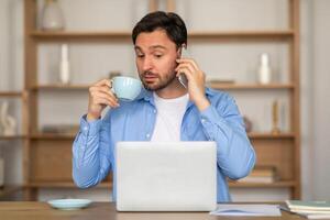 A man is standing with a cup of coffee in hand, engaged in a conversation on his phone. He appears focused on the call as he holds the phone to his ear. photo