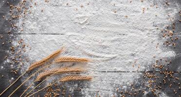 Baking class or recipe concept on dark background, sprinkled wheat flour, grain and ears with free copy space. Top view on wooden board or table. Cooking dough or pastry. photo