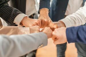 A group of business professionals in formal attire stand in a circle and bump fists as a symbol of unity and agreement, closeup, cropped photo