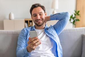 A man is sitting on a couch, engaged with his smartphone. He is focused on the devices screen, appearing absorbed in whatever content is displayed. photo