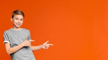 Cute little boy pointing away at empty space on orange studio background photo