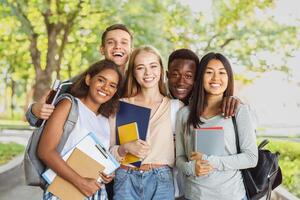 Group of international happy students with books and notebooks having fun in park after studying, smiling at camera photo