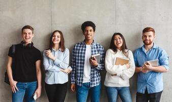College students with books smiling to camera over grey wall, having break photo