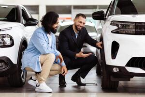 Two men are inspecting a car closely inside a well-lit showroom. One man is pointing at the features while the other is listening attentively. The car appears sleek and modern photo