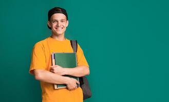 Happy student with books and backpack over turquoise background, copy space photo