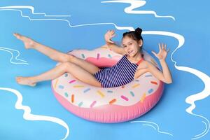 A young girl, wearing a swimsuit, is lying on an inflatable donut float in illustrated swimming pool. The girl seems relaxed and content as she floats on the colorful donut. photo