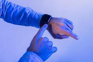 Man interacts with their smartwatch, using their finger to navigate through notifications or options. The ambient blue light gives the scene a futuristic and modern feel, cropped photo