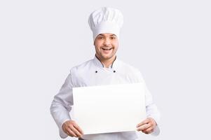 Smiling Chef Man Holding Blank Poster For Text Recommending Recipes Standing Over White Background. Studio Shot, Mockup photo
