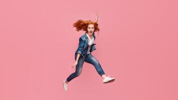 Redhead girl screaming and jumping in air on pink studio background photo